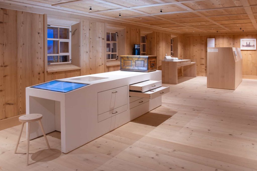 Interaktiver Museumsraum mit Touchscreen, geöffneter Schublade und barocker Truhe.