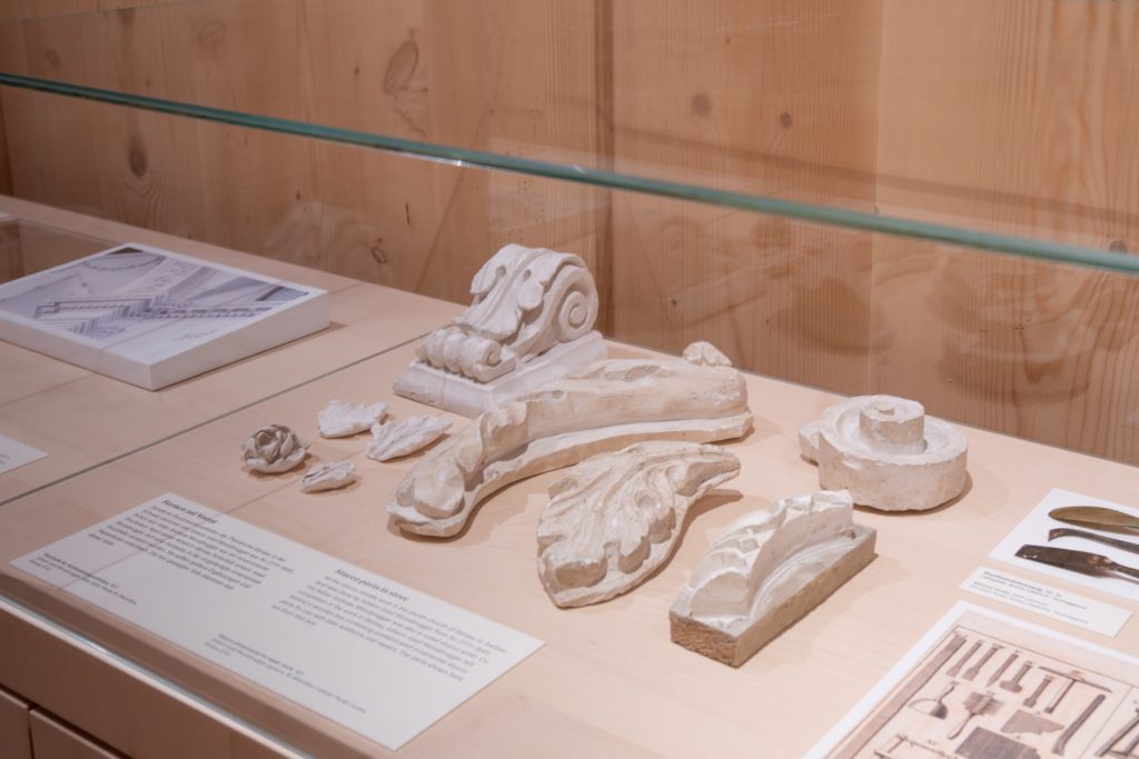 Gipsmodelle barocker Ornamente in Vitrine, mit Infotafeln und Architekturzeichnung.